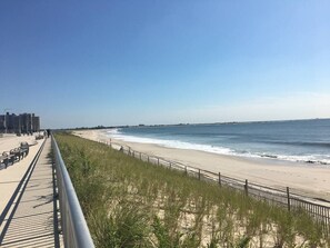 Une plage avec une promenade en bord de mer, des dunes herbeuses et un ciel dégagé.
