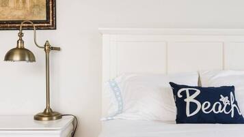 A bedroom with a white bed, a nightstand with a lamp, and two floral paintings on the wall.