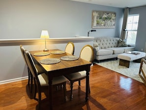 Un comedor con una mesa y sillas de madera, un sofá y un cuadro en la pared.