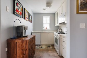 Une cuisine compacte avec des meubles blancs, une cuisinière, un évier et une machine à café posée sur un meuble en bois.