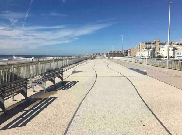 Un paseo marítimo con bancos, cielo despejado y edificios al fondo.