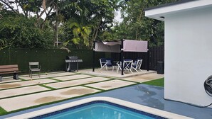 A backyard with a swimming pool, a barbecue grill, and outdoor furniture.