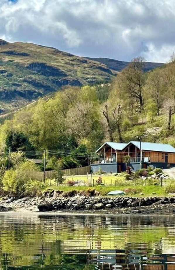 Eine Holzhütte am See mit Blick auf Berge, umgeben von Bäumen und einer Holzterrasse.