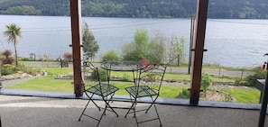 Un balcon avec une table et des chaises en métal, donnant sur un lac et une végétation luxuriante.