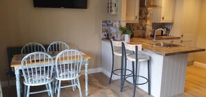 Une cuisine équipée d’une table à manger et de chaises, d’un tabouret de bar et d’un téléviseur fixé au mur.