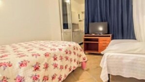 A bedroom with two beds, a television on a wooden stand, and a mirror.
