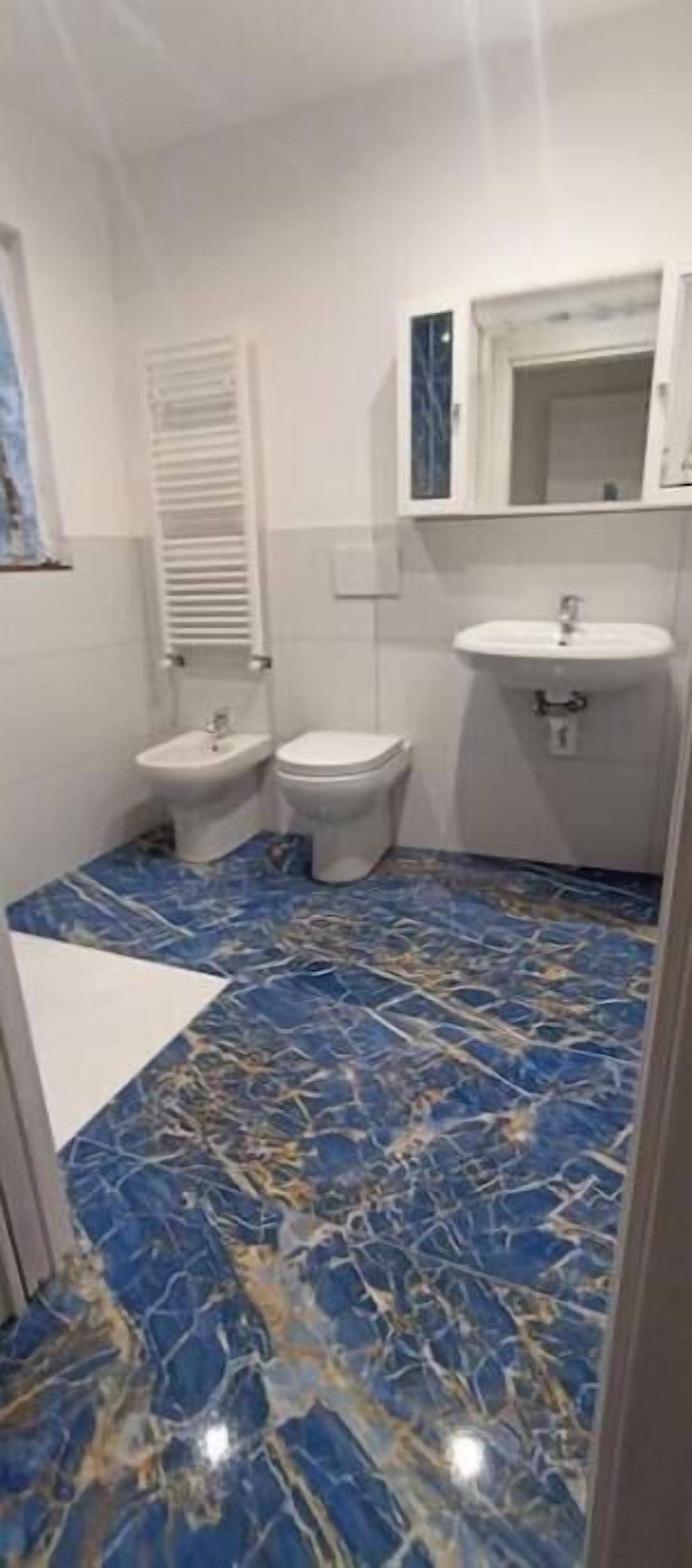 Un baño con piso de mármol azul, lavamanos blanco, inodoro y bidé.