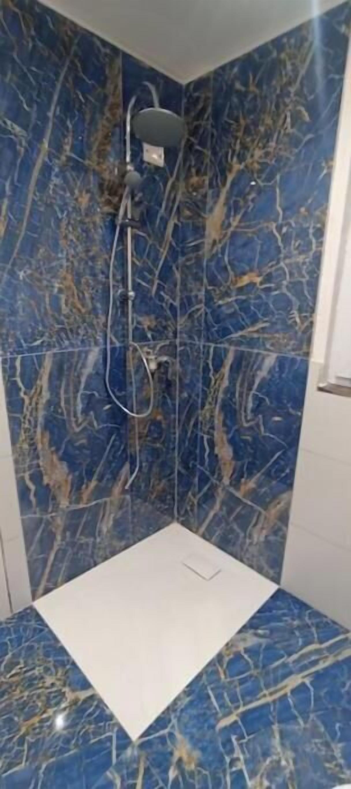 Eine Dusche mit weißem Boden und Wänden, und einem blauen Marmormuster.