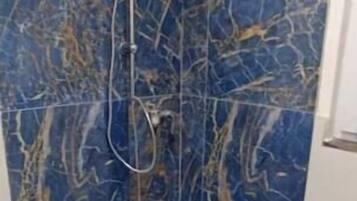 Eine Dusche mit weißem Boden und Wänden, und einem blauen Marmormuster.