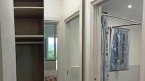 A narrow hallway leading to a bedroom with a bed and a bathroom with a shower curtain.