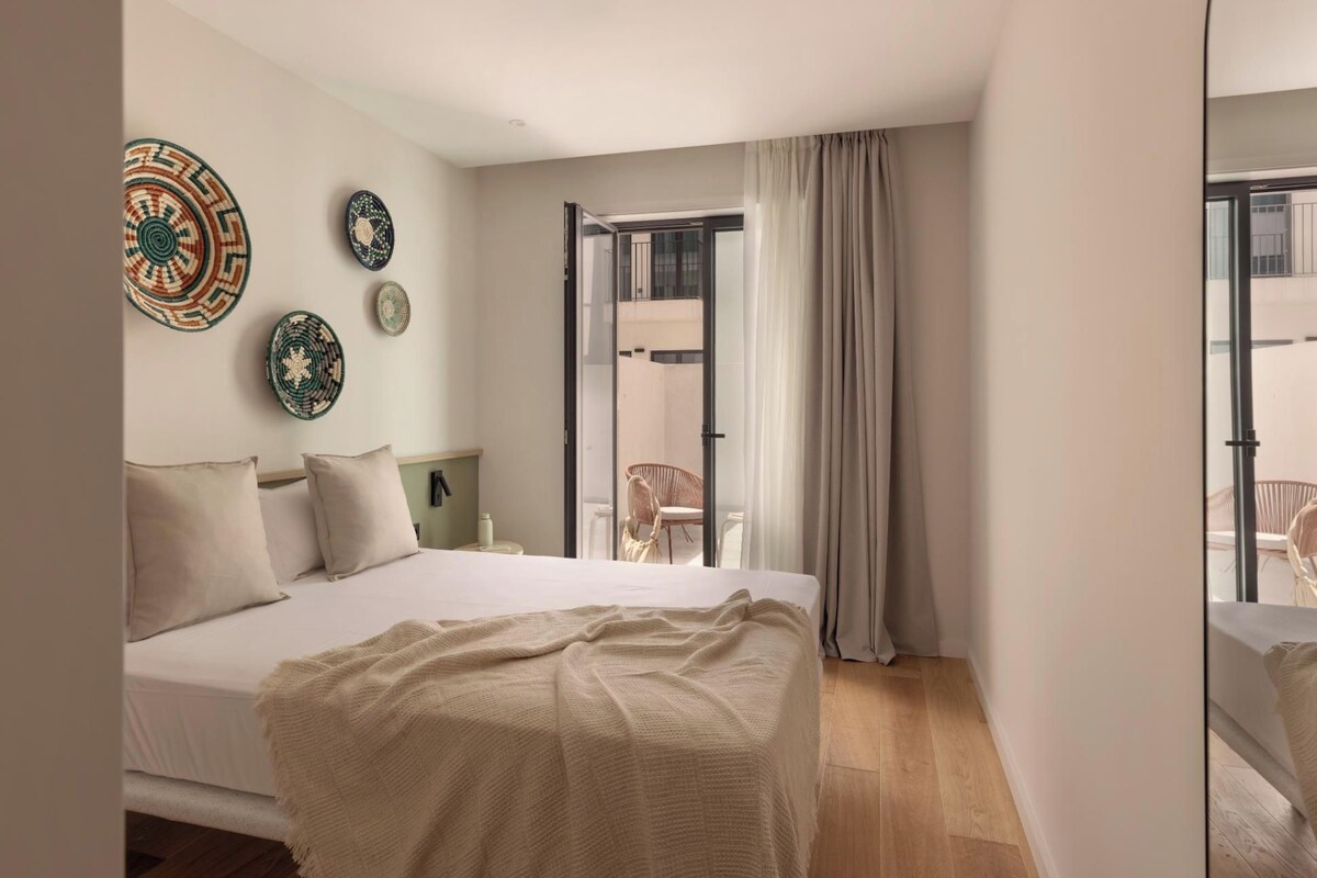 A bedroom with a bed, a nightstand, a mirror, and a view of an outdoor balcony.