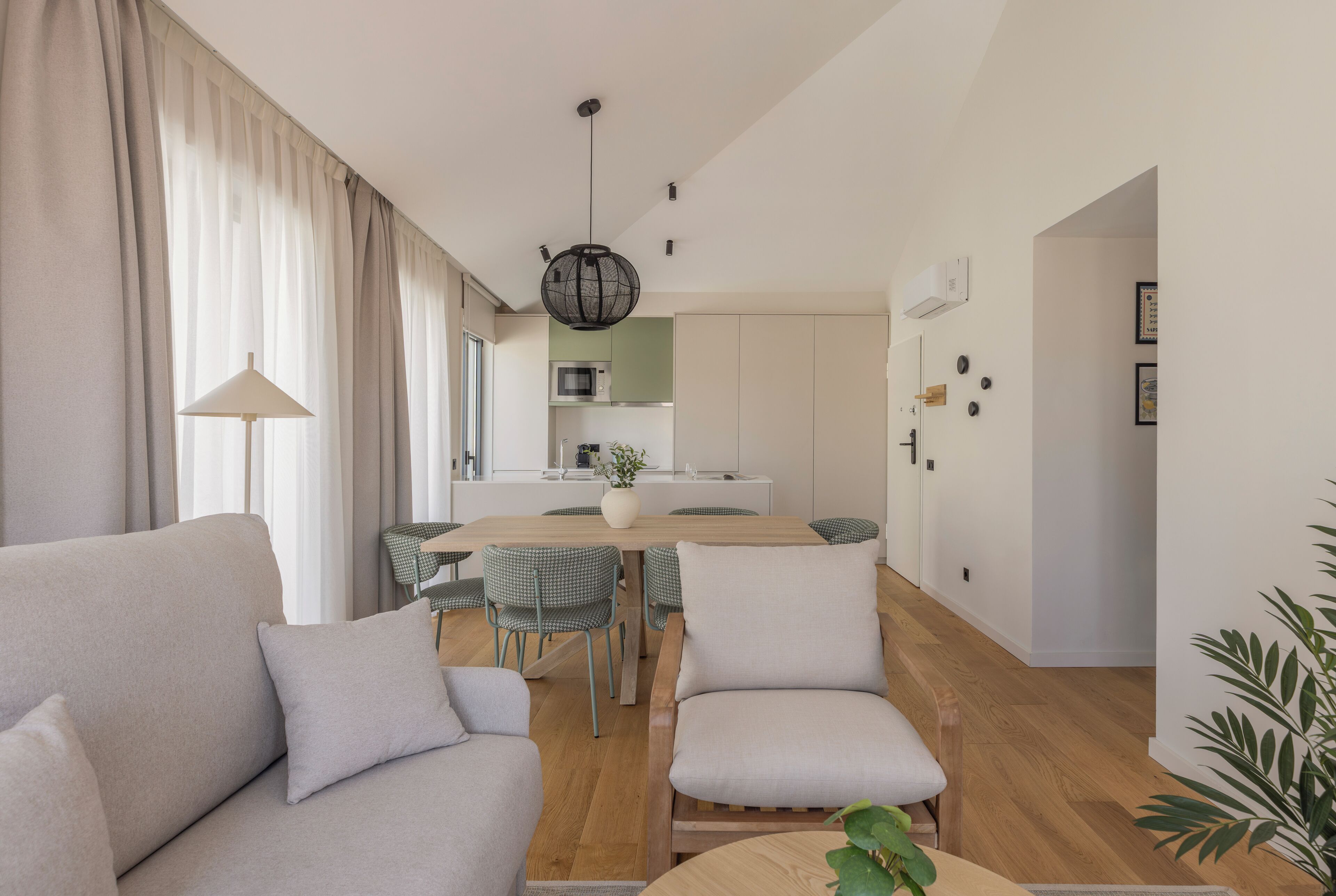 A modern living room with a sofa, chairs, a dining table, and a kitchen in the background.