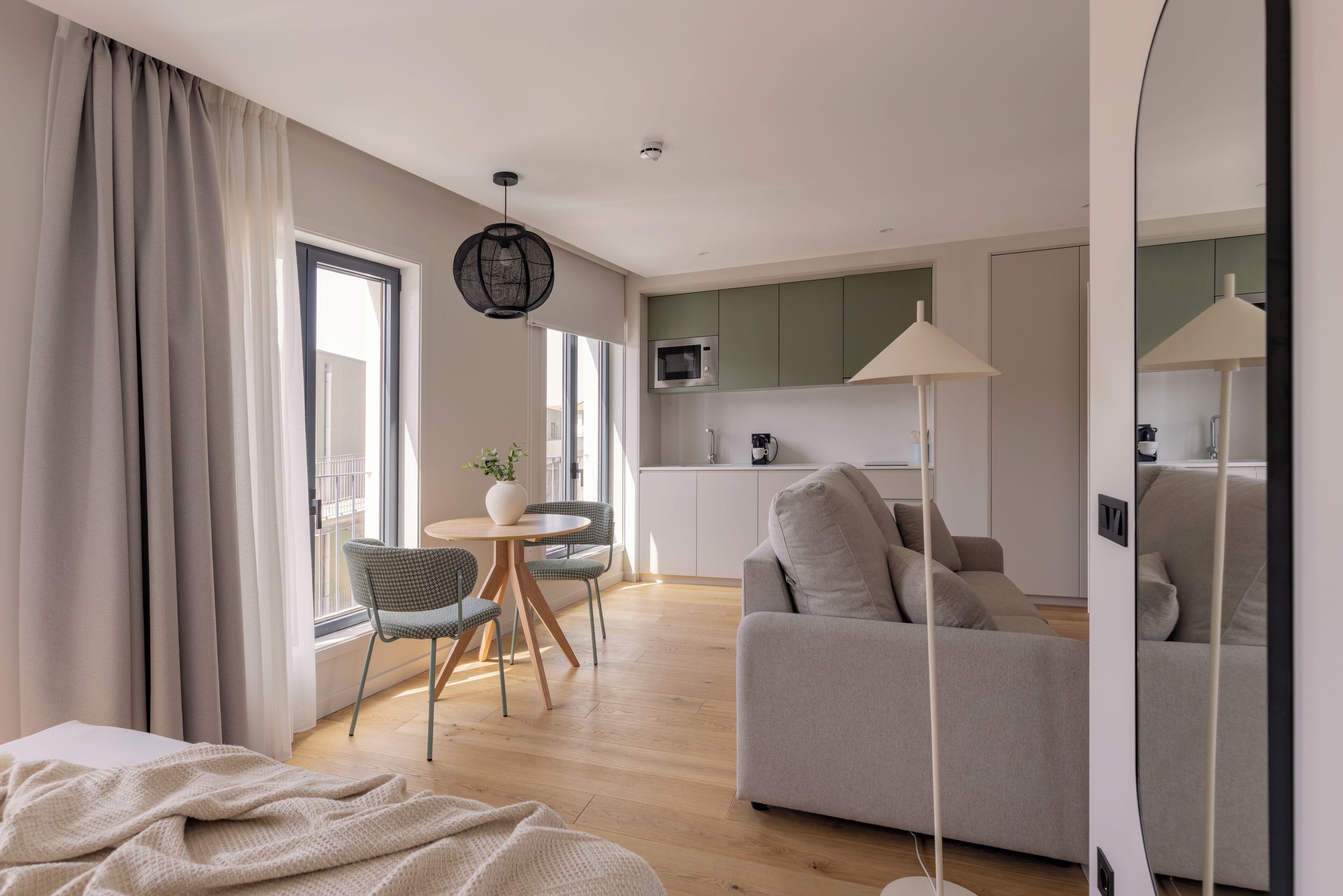 Ein modernes Wohnzimmer mit einer Couch, einem Essbereich mit Stühlen, einer Küche mit Schränken und einem großen Fenster.