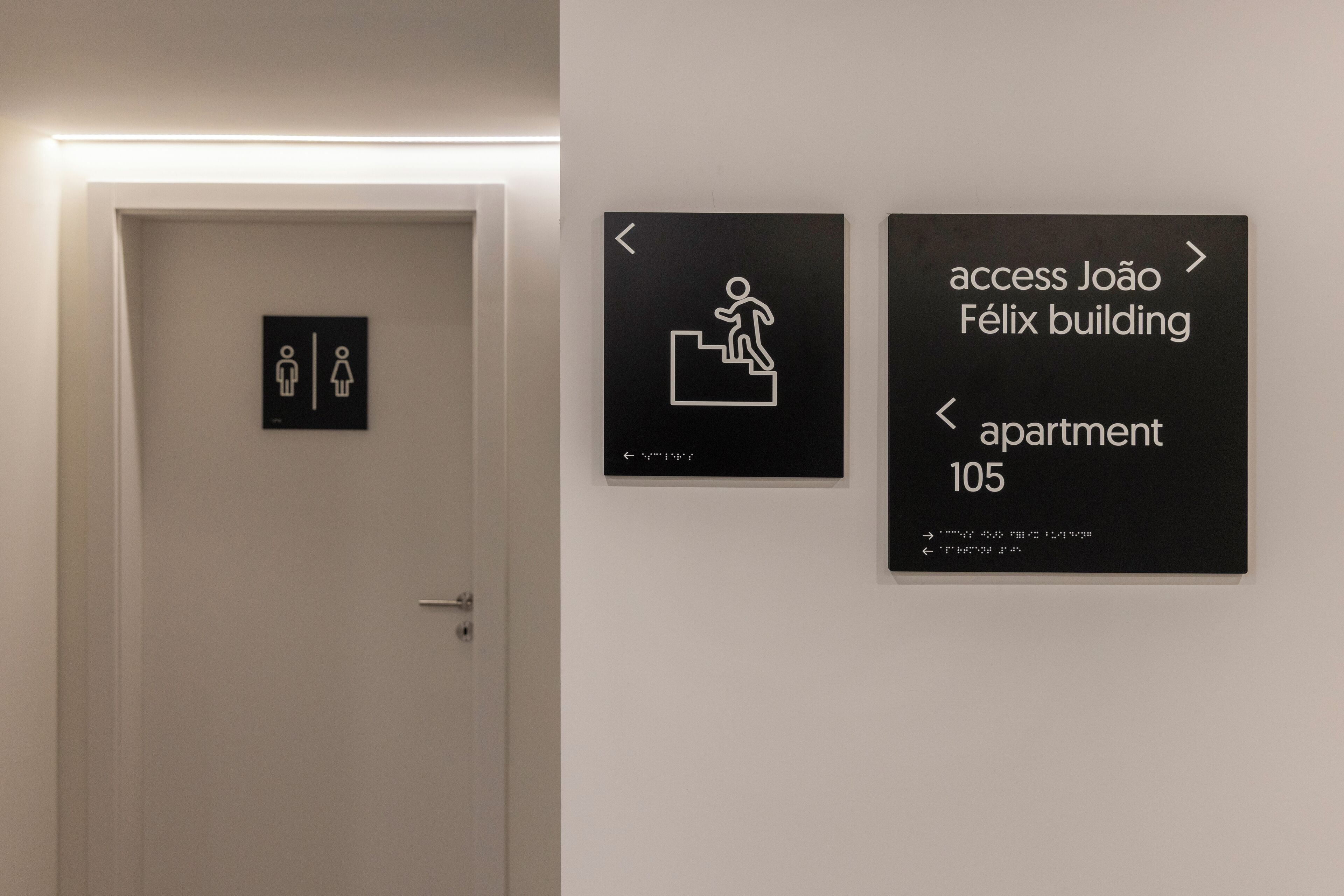 A door with a gender-specific restroom sign and directional signs for João Félix building and apartment 105.