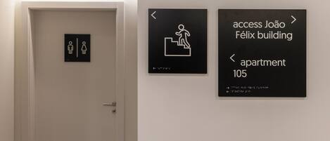 A door with a gender-specific restroom sign and directional signs for João Félix building and apartment 105.