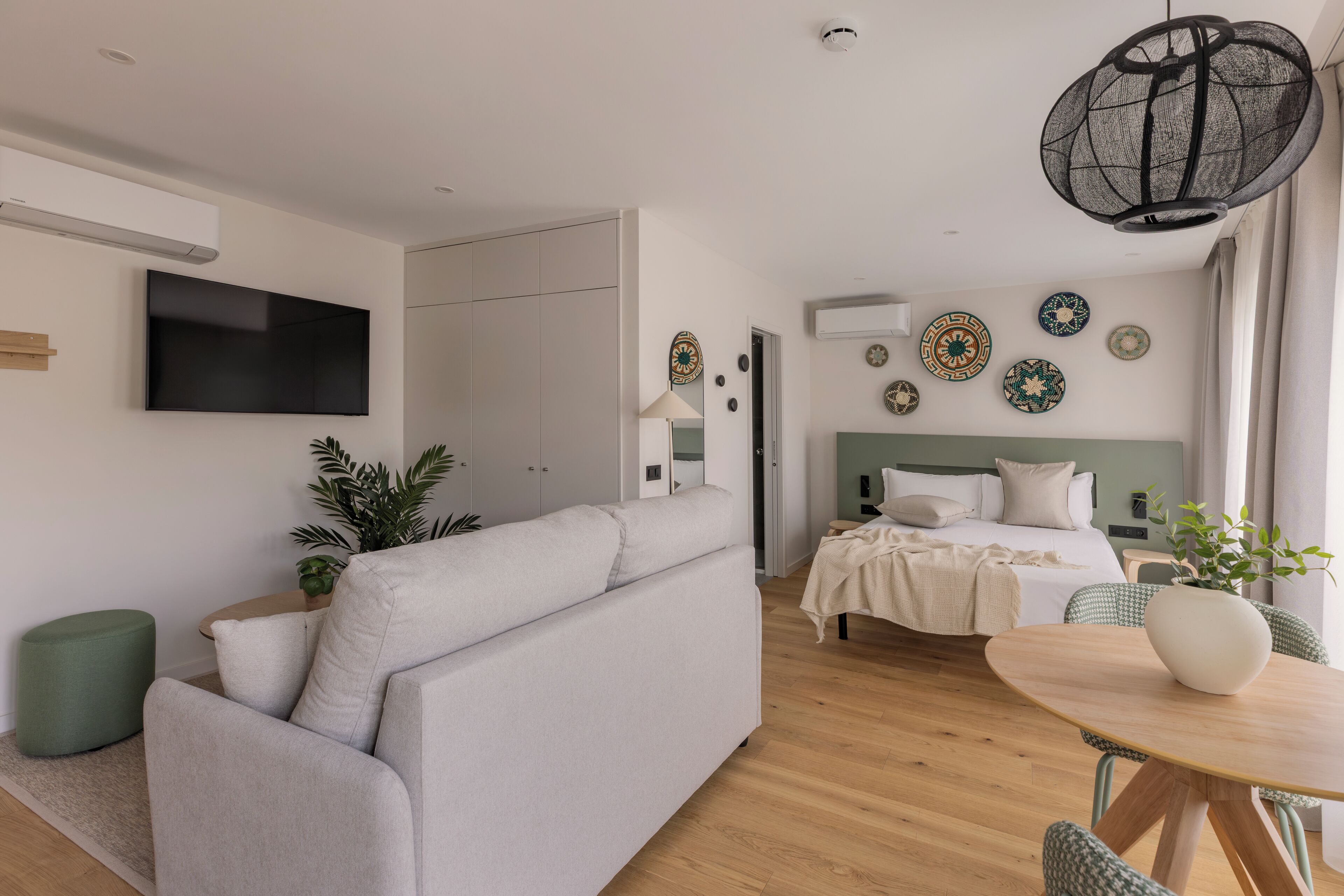 Una habitación de hotel moderna con sofá, cama, televisor, mesa de comedor y platos decorativos en la pared.