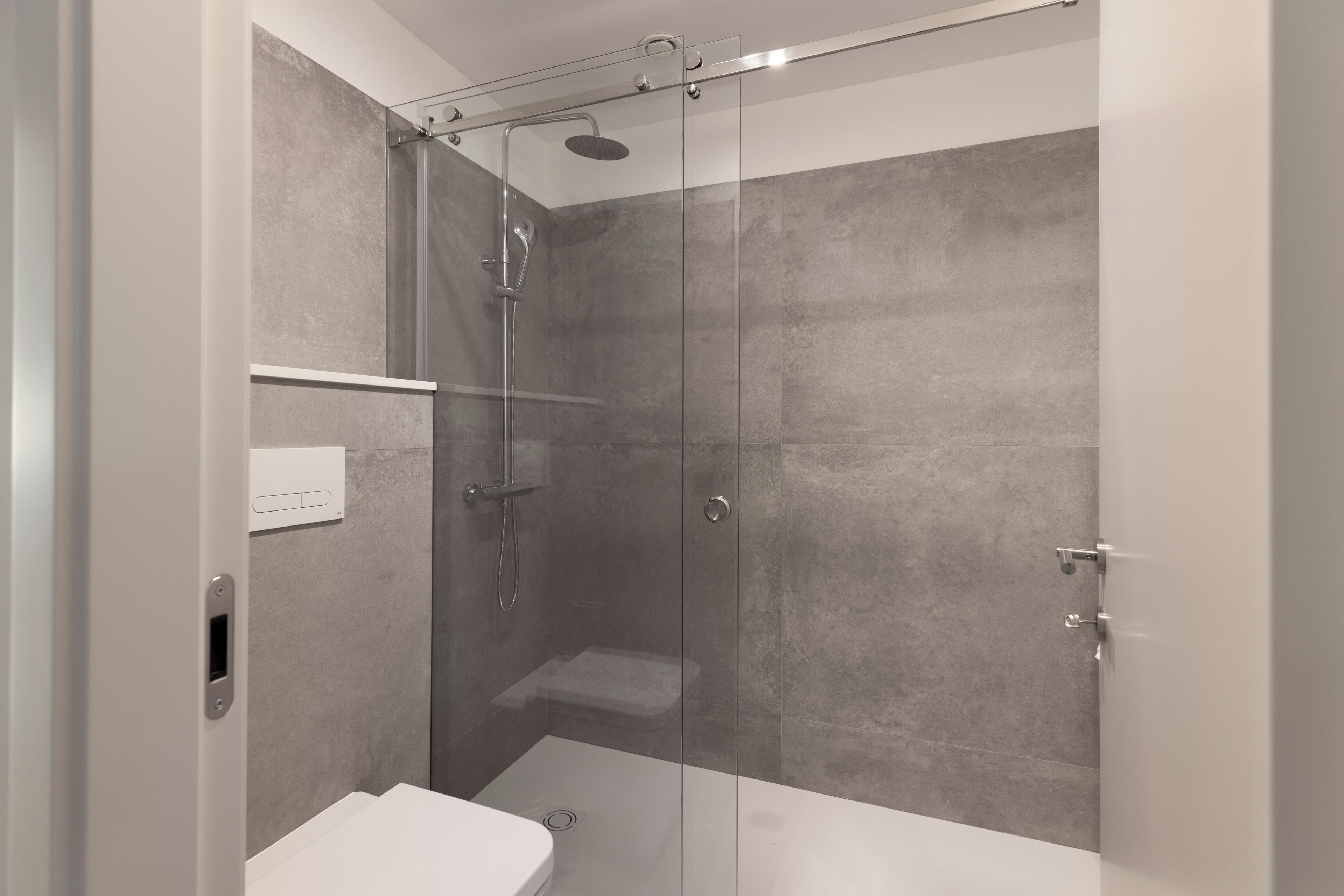 Une salle de bain moderne avec une douche à parois de verre, des toilettes blanches et une prise électrique visible.