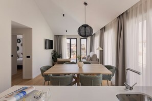 A modern dining area with a wooden table, wicker chairs, a vase, and a view of the city through large windows. - Libere Porto Gaia (Vila Nova de Gaia)