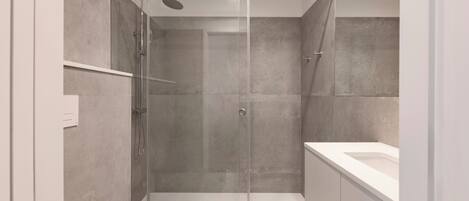 Un baño moderno con ducha de vidrio, un lavabo blanco y un armario.