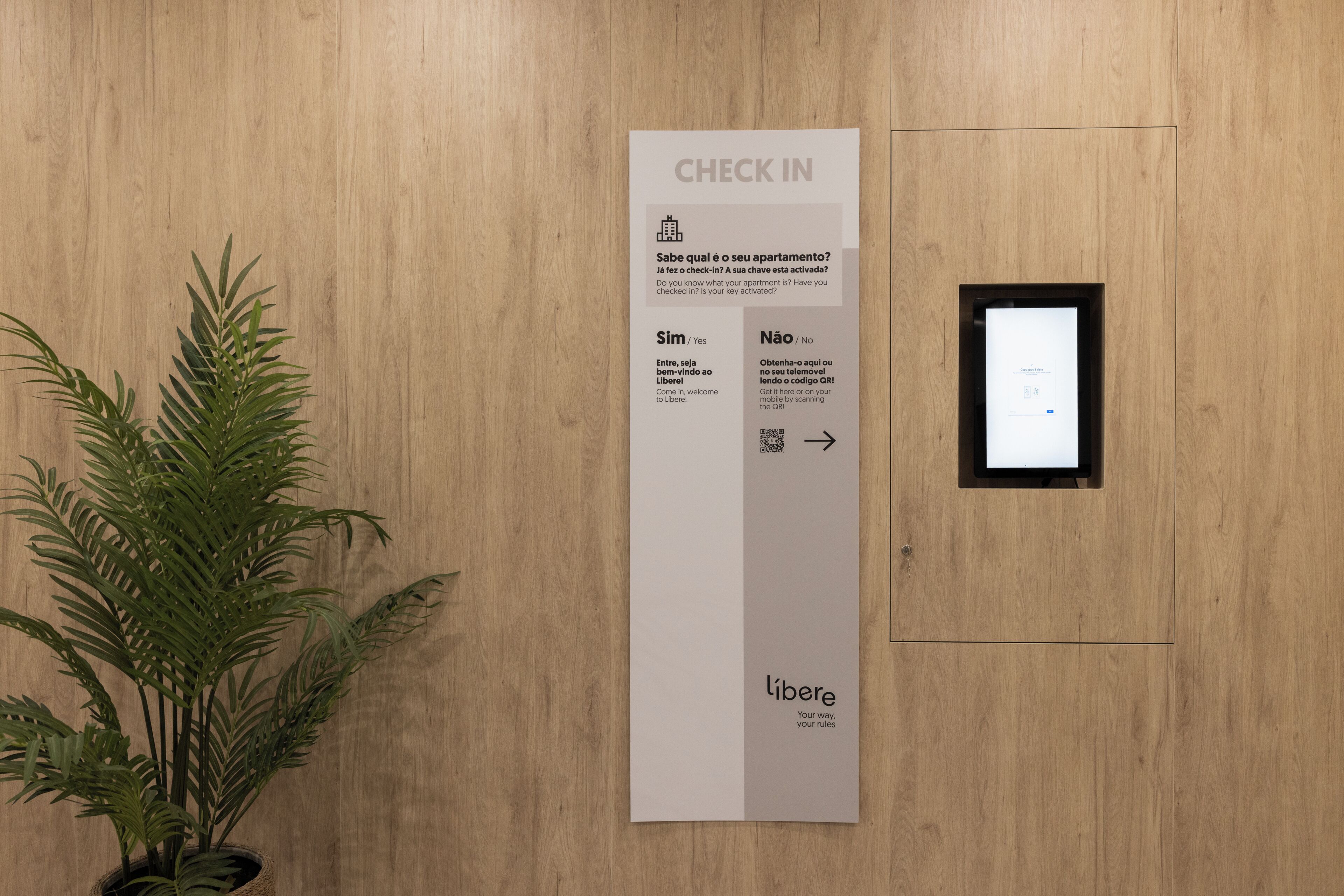 A check-in sign with a QR code, a potted plant, and a wooden wall.