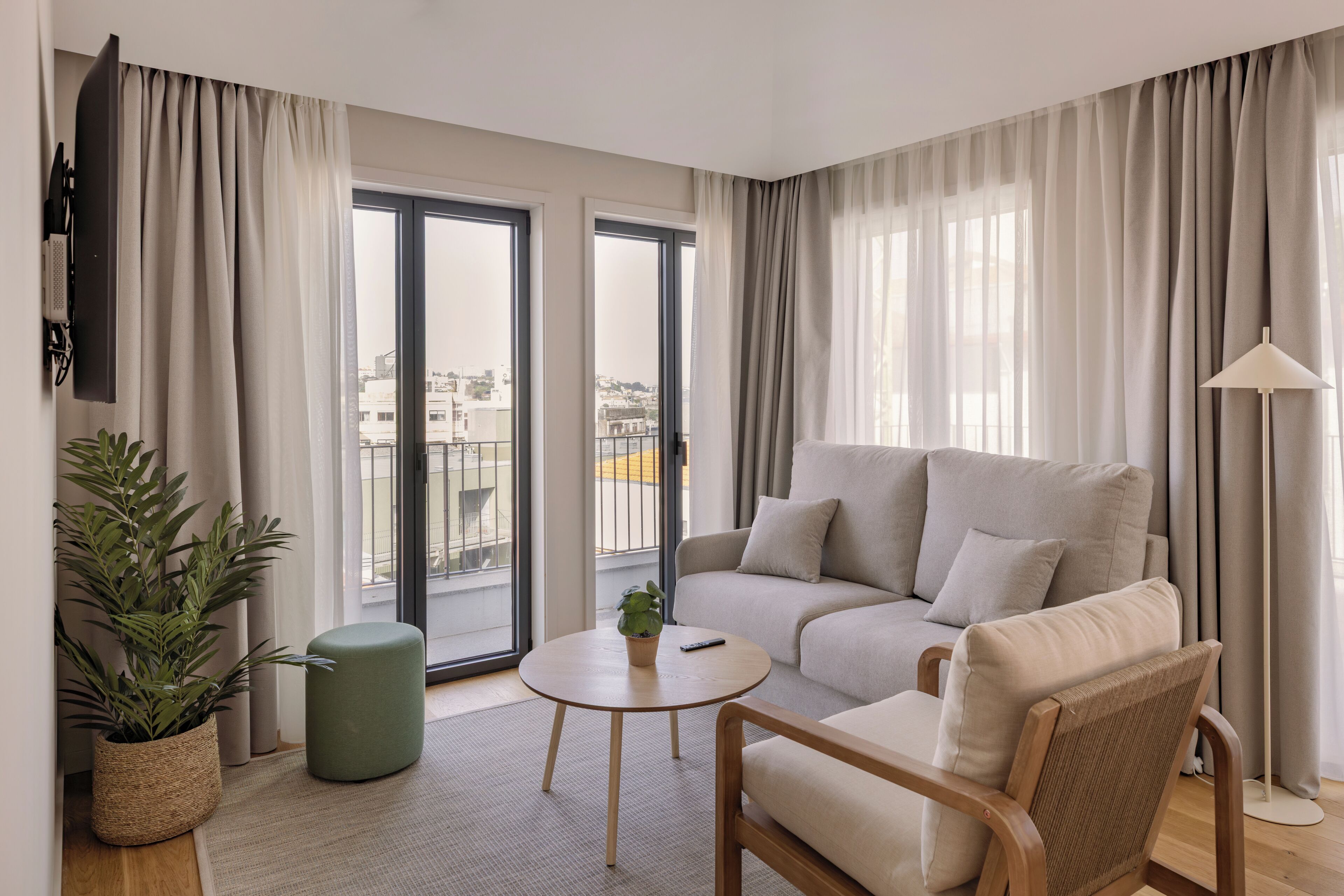 A modern living room with a sofa, a round table, a green ottoman, a potted plant, and a floor lamp.