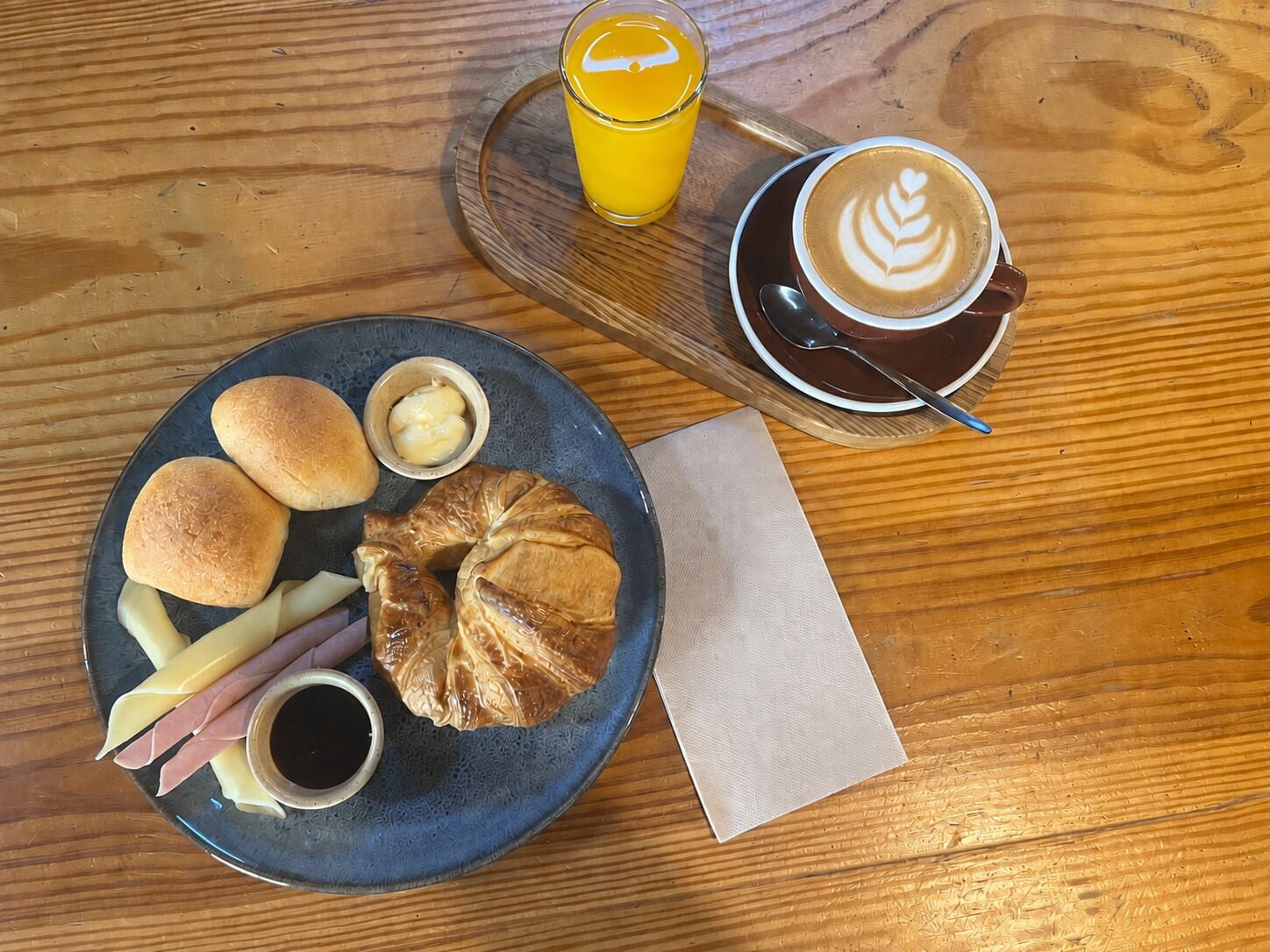 A breakfast tray with croissants, bread rolls, cheese, ham, and a small bowl of butter on a plate.
