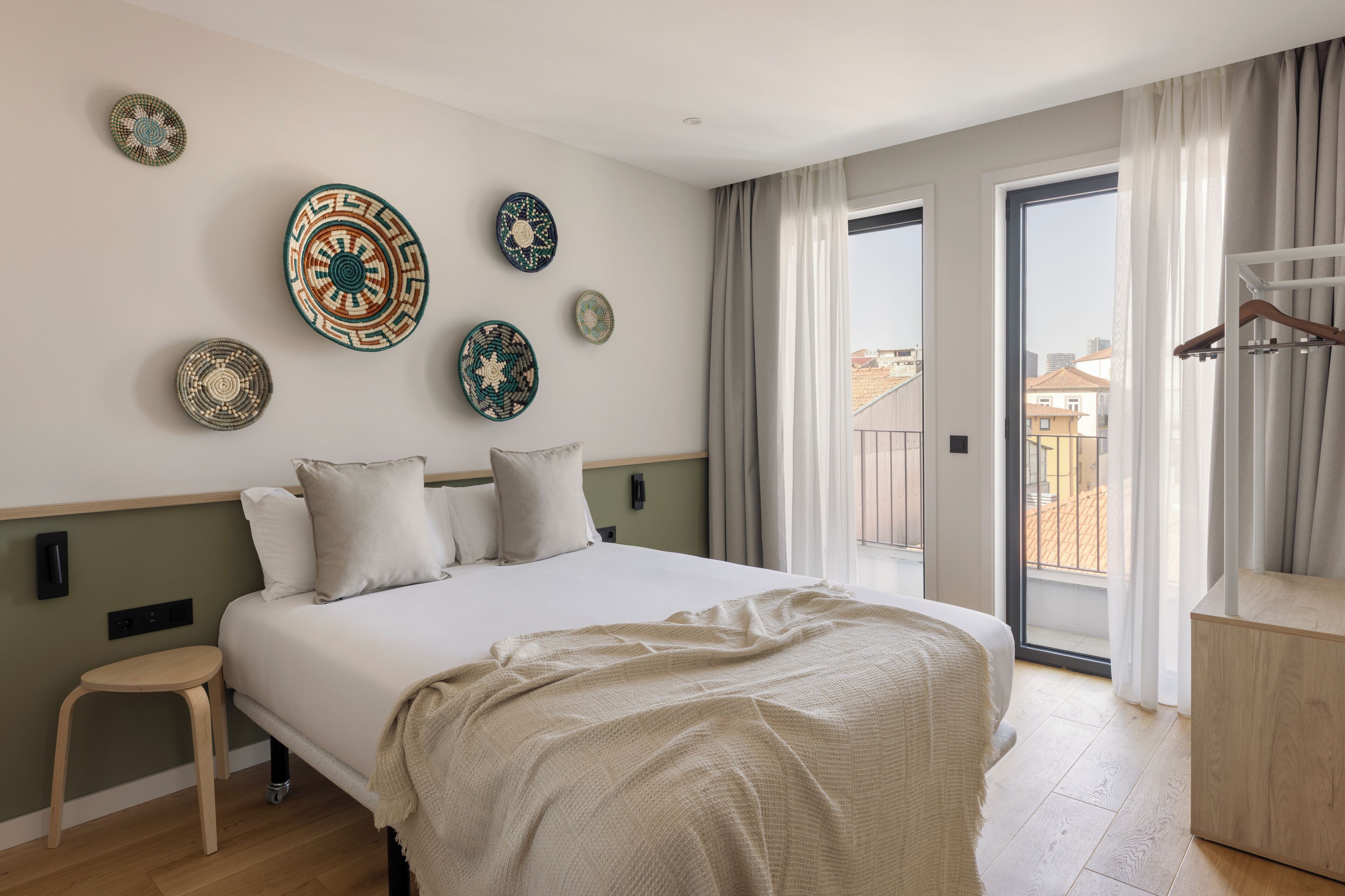 Un dormitorio con cama, un taburete de madera, un balcón con vistas y placas decorativas en la pared.