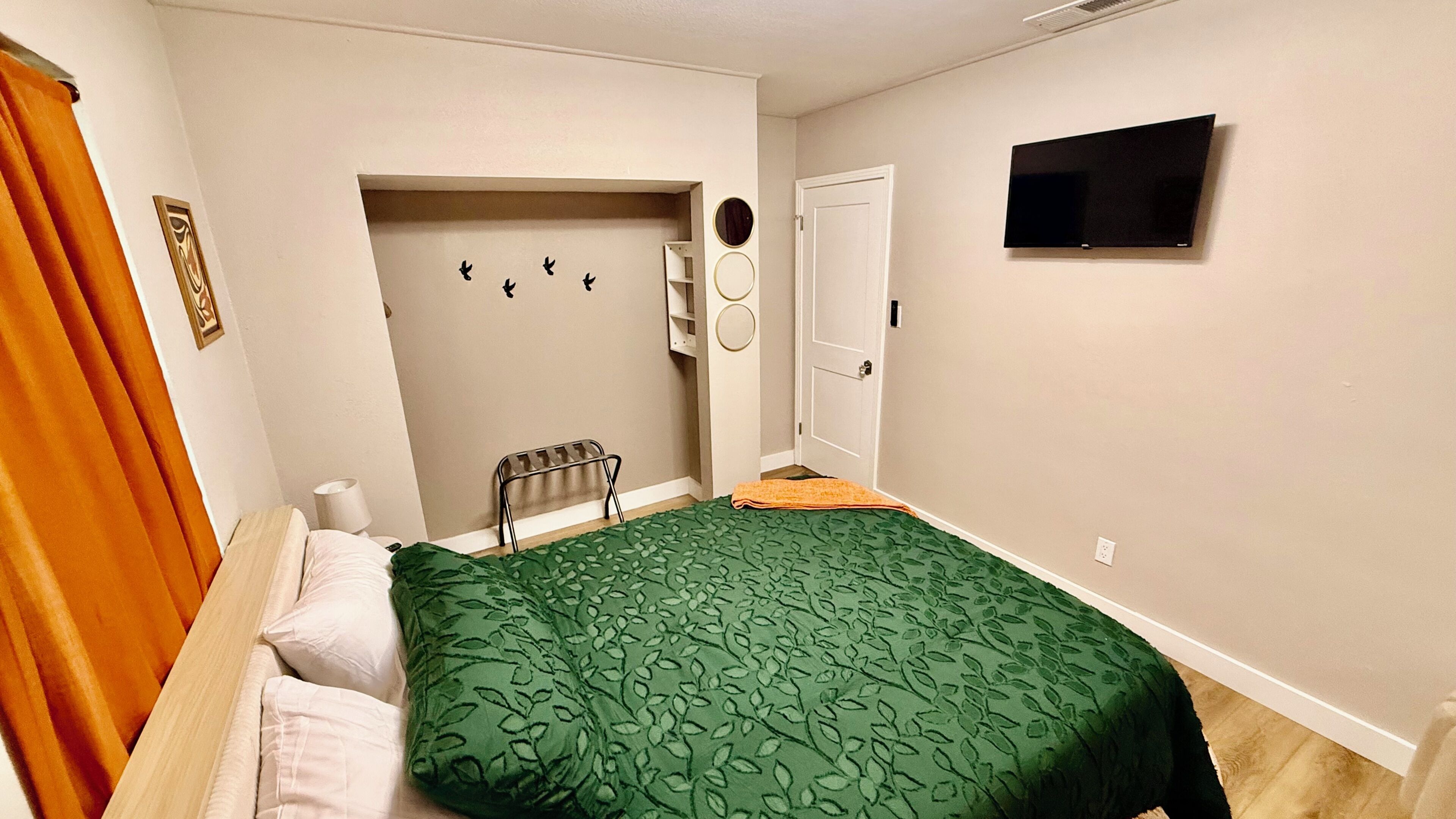 A bedroom with a bed, a TV, a door, and a small window.