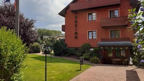 Un bâtiment rouge avec le nom « TENZIO » inscrit sur le côté, un chemin pavé et un petit espace extérieur aménagé avec des sièges.