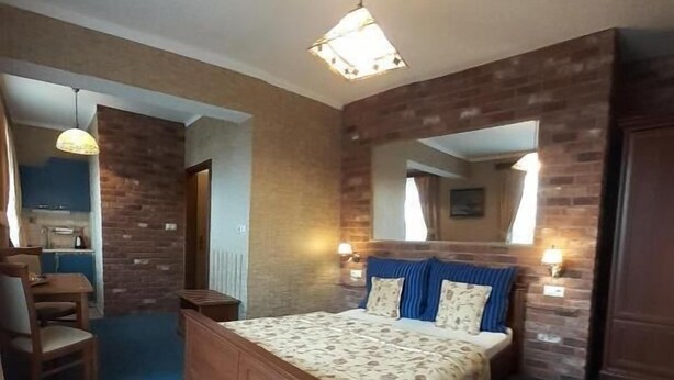 Une chambre avec un grand lit, une tête de lit en bois, une moquette bleue et un mur en briques.