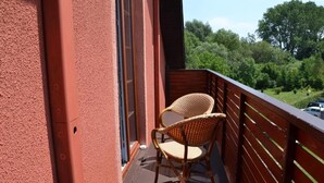 Un balcon avec un fauteuil en osier, une balustrade en bois et une vue sur la verdure.