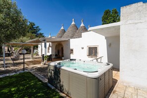 A spa area with a hot tub, outdoor seating, and a white building with conical roofs. - Trulli Valeria by Monholiday (Monopoli)