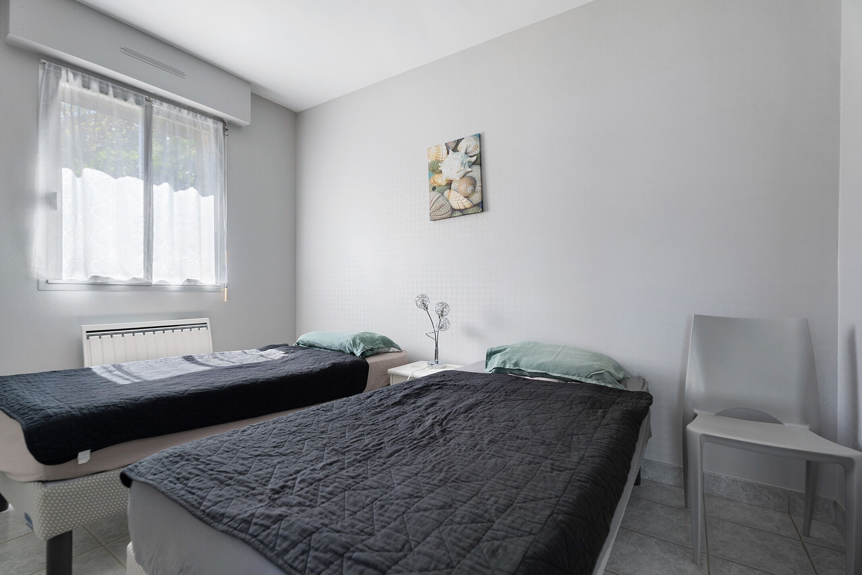 Une chambre avec deux lits, une chaise, un radiateur et une fenêtre avec des rideaux.