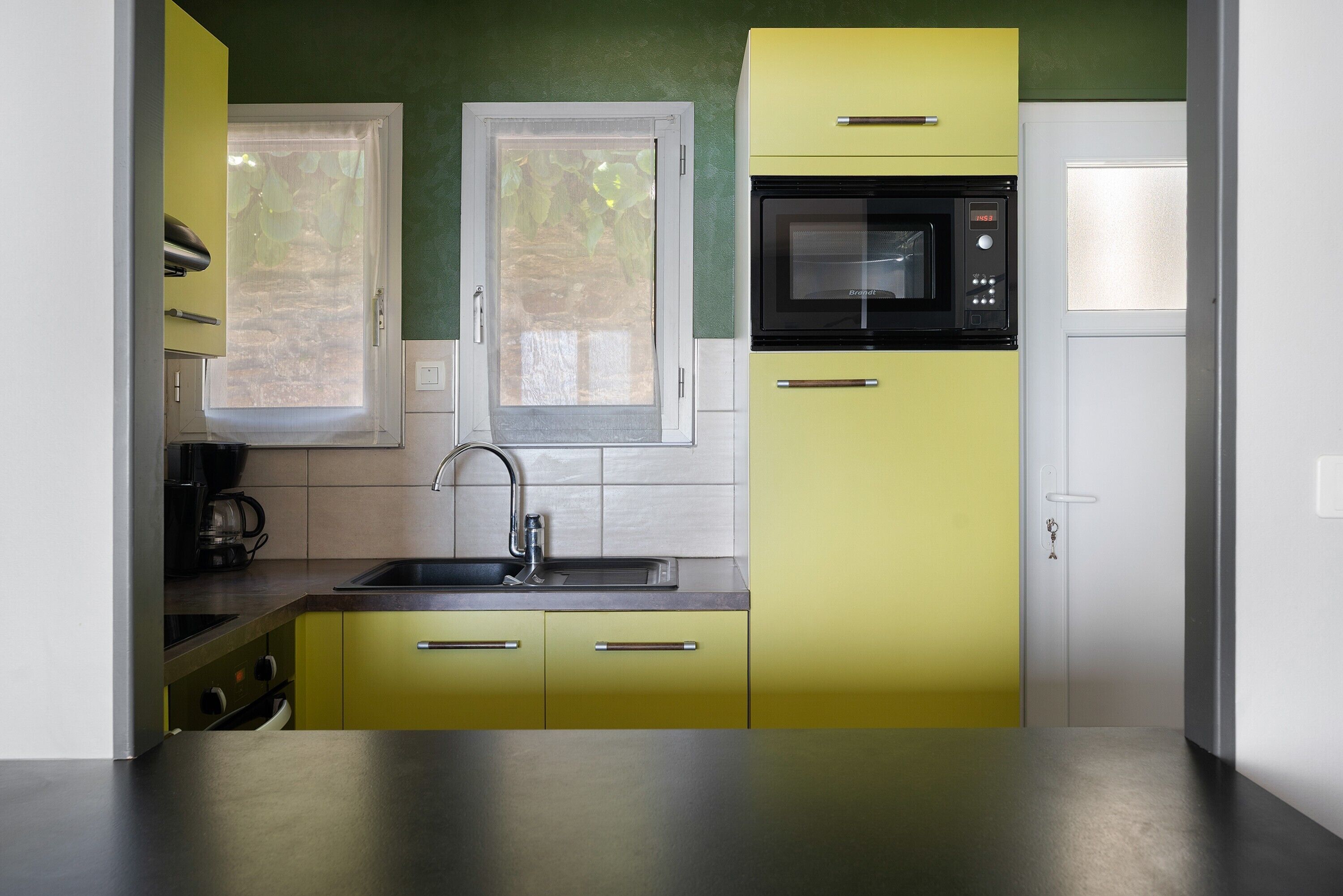 Una cocina con armarios amarillos, encimera de acero inoxidable, microondas y ventana con vistas al verdor.
