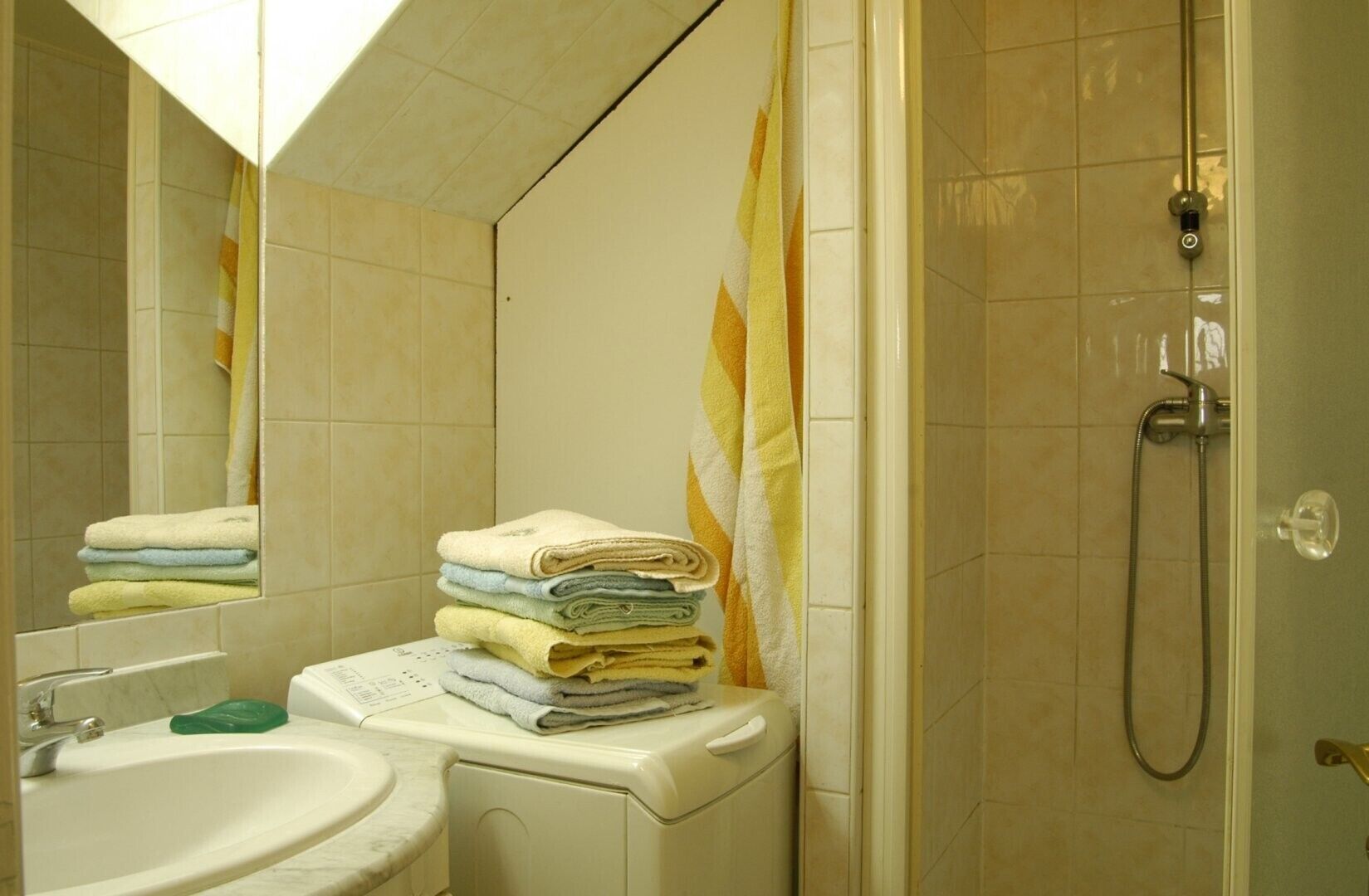 A bathroom with a sink, stacked towels, a shower, and a mirror.
