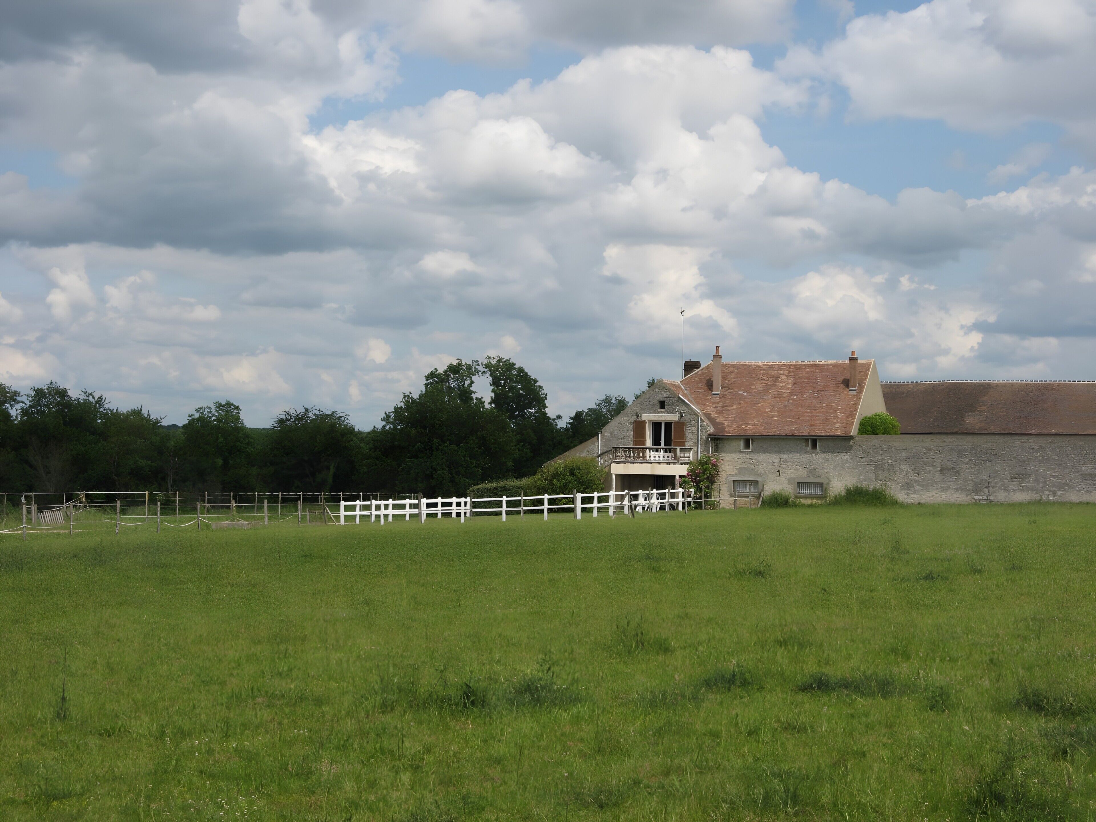 Een landhuis met een stenen muur, een wit hek en een grasveld.