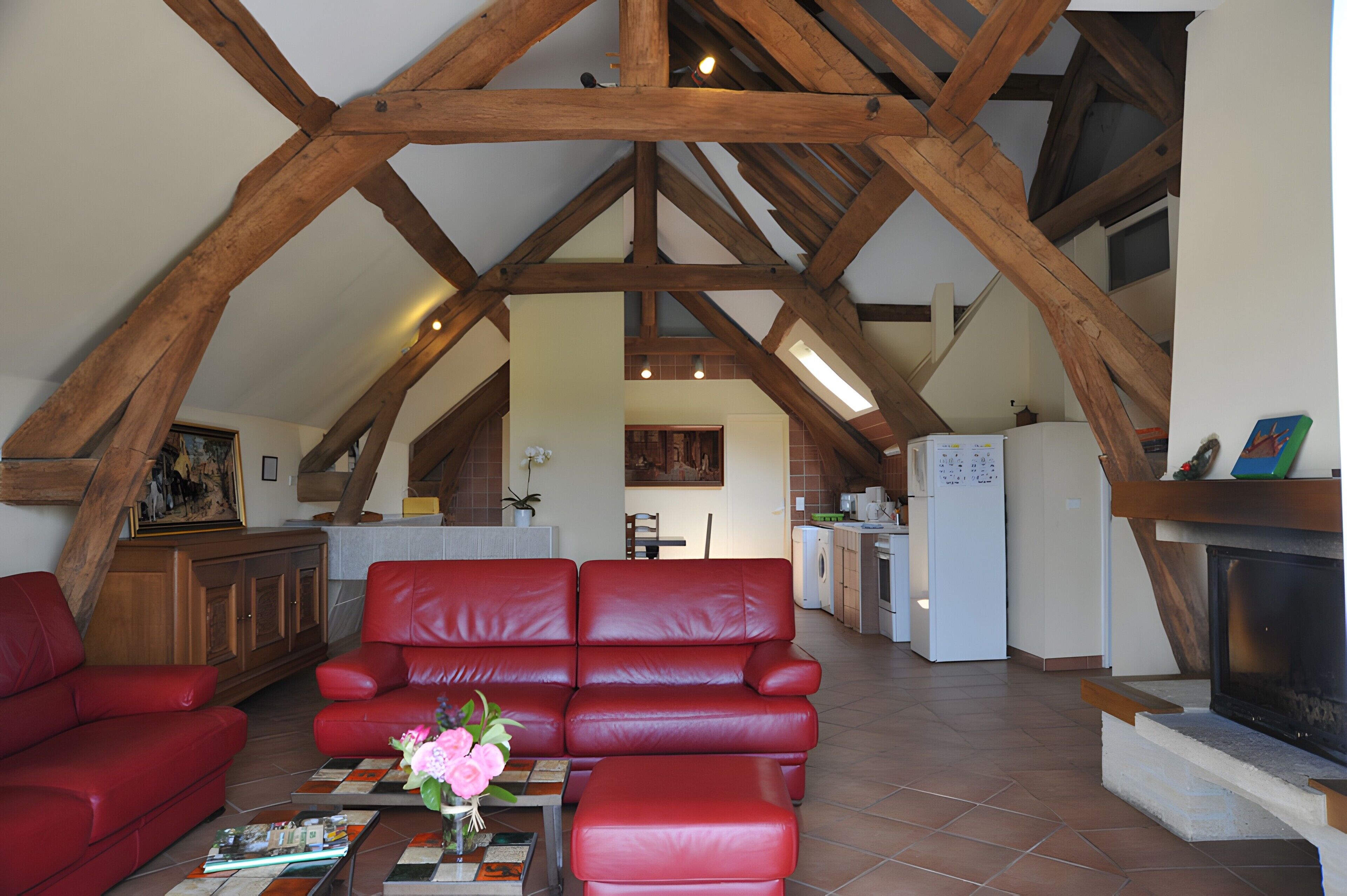 A loft-style living area with a red leather sofa, a fireplace, and exposed wooden beams.