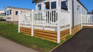 En campingvogn med en indhegnet terrasse, en lille veranda og en paraboldish.