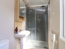 A bathroom with a glass-enclosed shower, a white sink, and a wooden shelf.