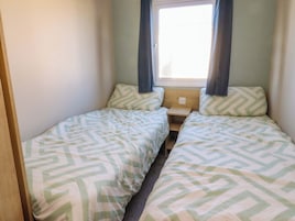 Un alojamiento pequeño de una sola habitación con dos camas, una ventana con cortinas y una mesita de noche de madera.