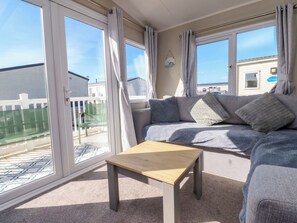 Ein gemütliches Wohnzimmer mit einer Couch, einem Holztisch und großen Fenstern.
