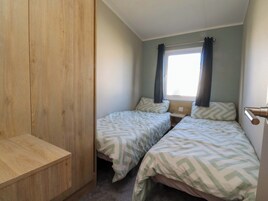 Habitación pequeña con dos camas individuales, un armario de madera, una mesita de noche y una ventana con cortinas.