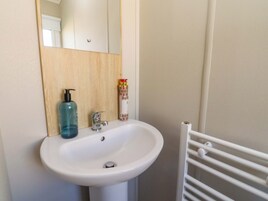 Un baño con un lavamanos blanco, un espejo, un panel de madera, una botella de jabón líquido y un radiador blanco.