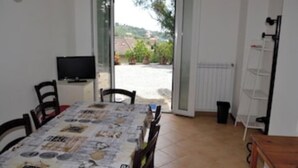 Un comedor con una mesa cubierta por un mantel, sillas, un televisor y vistas al exterior.