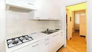 Una cocina compacta con armarios blancos, estufa a gas y pileta.