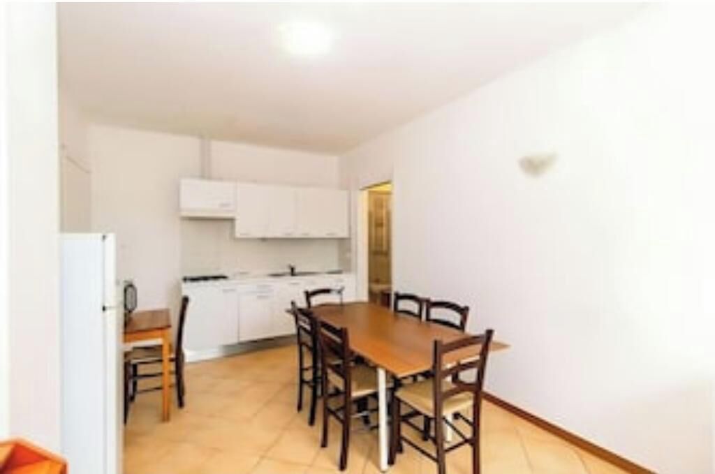 A compact kitchen with white cabinets, a dining table with chairs, and a small refrigerator.
