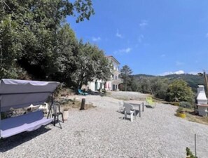 A gravel courtyard with a covered seating area, a building in the background, and surrounding trees. - Sun Apartment in Villa Daria 2 km from the sea of the Gulf of Tigullio (Chiavari)