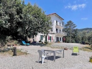 A two-story building with a balcony, surrounded by trees and a gravel area with outdoor furniture. - Sun Apartment in Villa Daria 2 km from the sea of the Gulf of Tigullio (Chiavari)