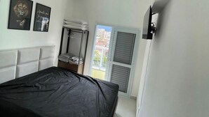 A bedroom with a bed, a wardrobe, a window with shutters, and a wall-mounted TV. - Villa Bellagio (Ubatuba)