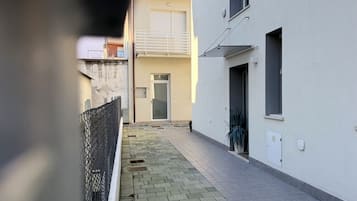 Uma viela estreita com um edifício branco à direita, uma porta e uma pequena janela.
